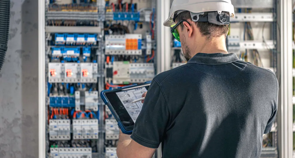 Technician reviewing electrical equipment with a tablet during a site inspection